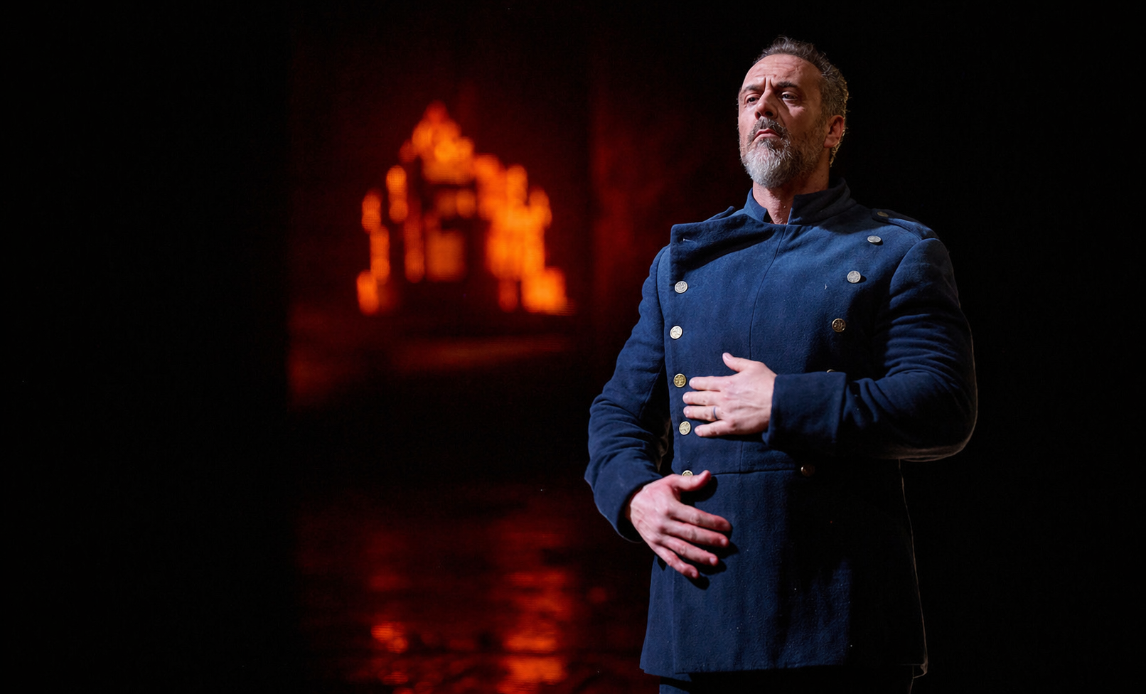 Christian Van Horn as Duke Bluebeard in a blue coat against red stage lighting in the Canadian Opera Company’s Bluebeard’s Castle.