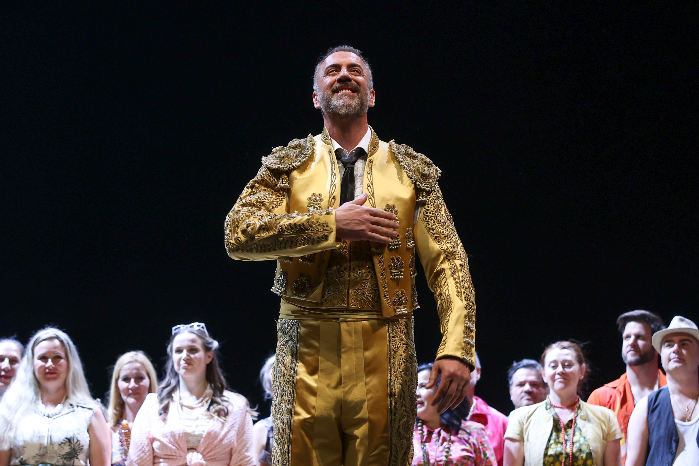 Christian Van Horn in a gold Escamillo costume onstage at Vienna State Opera, smiling with one hand over his heart.