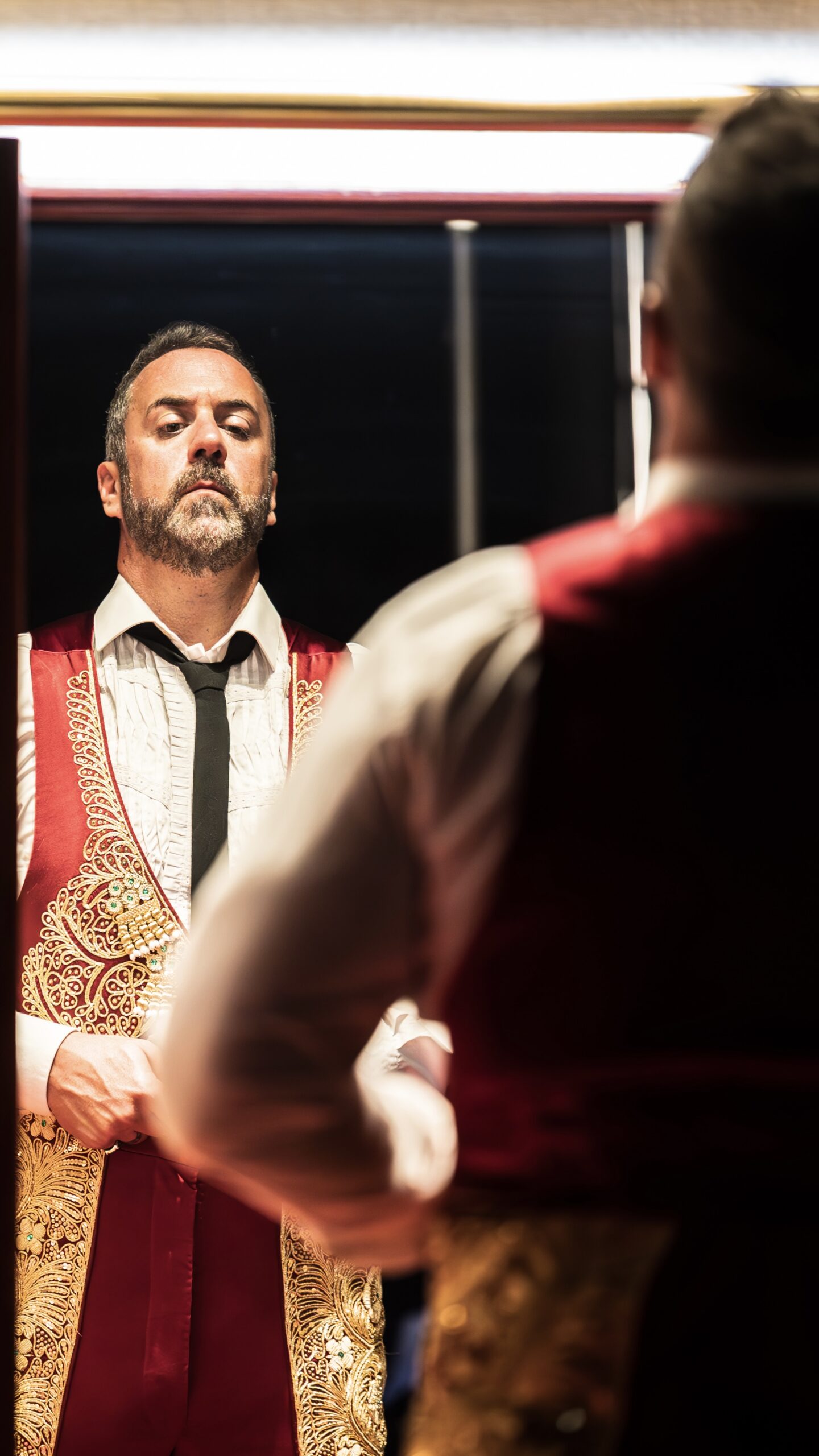 Christian Van Horn as Escamillo looks into a dressing-room mirror in a red and gold costume.